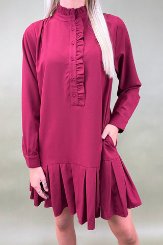 Maroon dress with long sleeves and ruffled details on a plain background