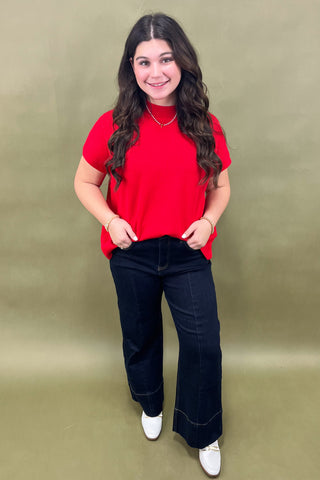 Woman wearing a red top and black pants against a green background