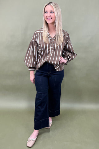 Woman wearing a striped blouse and dark jeans against a plain background