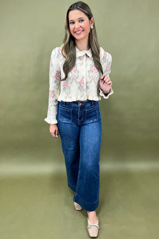 Woman wearing a floral blouse and blue jeans against a green background