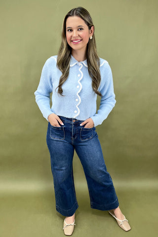 Woman wearing a light blue shirt with a white collar and dark blue jeans against a green background