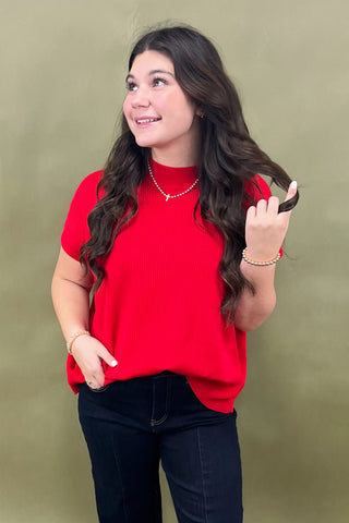 Woman wearing a red sweater and black pants against a green background