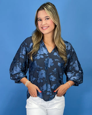 Navy blue floral textured blouse with a V-neck and three-quarter balloon sleeves, shown on model.