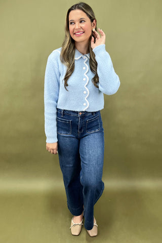 Woman wearing a light blue sweater and dark blue jeans on a green background