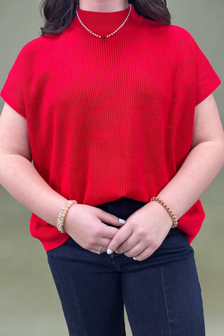 Person wearing a red top and dark jeans with a plain background