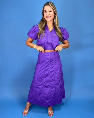 A woman modeling a purple two-piece set consisting of a short-sleeve button-up blouse with puffed sleeves and a matc