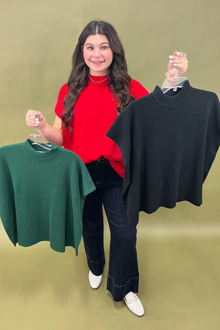 Woman holding a red sweater and two other sweaters on hangers against a green background