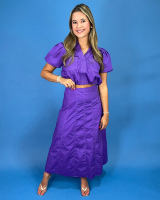 A woman modeling a purple two-piece set consisting of a short-sleeve button-up blouse with puffed sleev