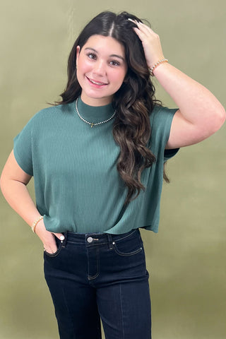 Woman wearing a green ribbed top and black jeans against a green background