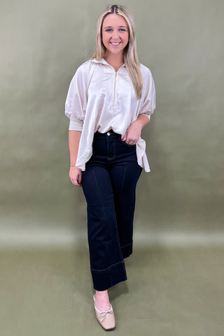 Woman wearing a white blouse and black pants against a green background