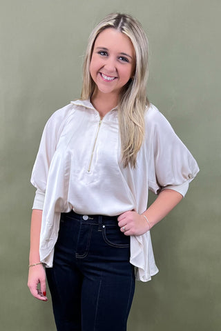 Woman wearing a white blouse with short sleeves and a zipper, standing against a green background