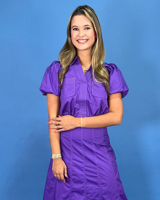 A woman modeling a purple two-piece set consisting of a short-sleeve button-up blouse with puffed sleeves and a matching ple