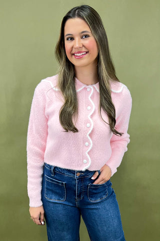Woman wearing a pink cardigan with white buttons against a green background