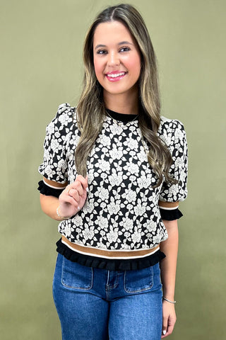 Woman wearing a black and white floral top with blue jeans against a green background
