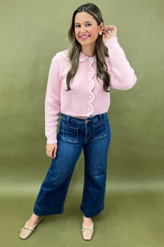 Woman wearing a pink sweater and blue jeans against a green background