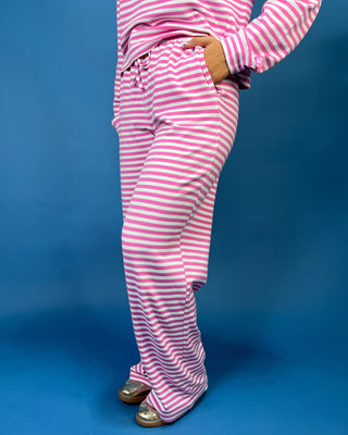 A woman modeling a pair of striped Lulu Mac Pink and White tie waist pants against a blue background. 