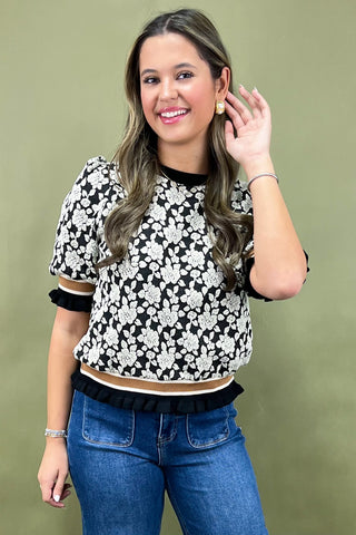 Woman wearing a black and white floral top with blue jeans against a green background