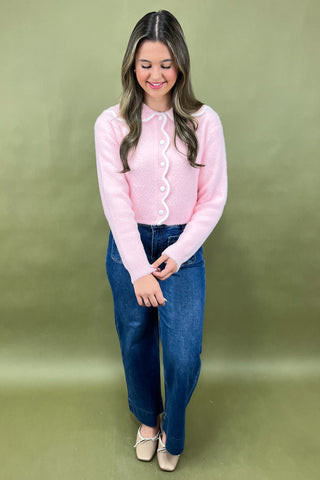 Woman wearing a pink blouse and blue jeans against a green background
