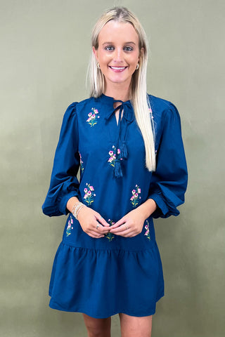 Woman wearing a blue dress with floral embroidery against a green background