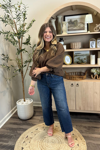 Woman standing in a room with a plant and a shelf in the background
