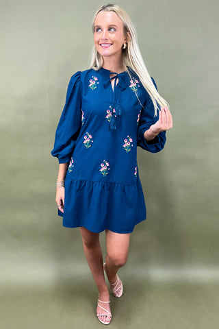 Woman wearing a blue dress with floral patterns against a green background