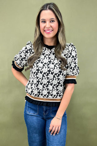 Woman wearing a black and white floral blouse with blue jeans against a green background