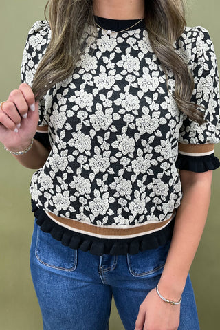 Person wearing a black and white floral blouse with ruffled details on a green background