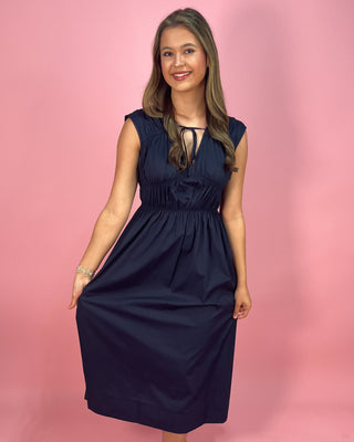 Woman wearing a navy blue dress against a pink background