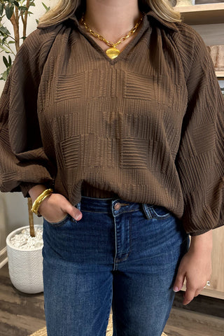 Person wearing a brown textured blouse and blue jeans indoors.