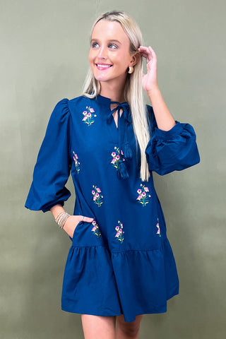 Woman wearing a blue dress with floral embroidery against a green background