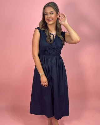 Woman wearing a navy blue dress against a pink background
