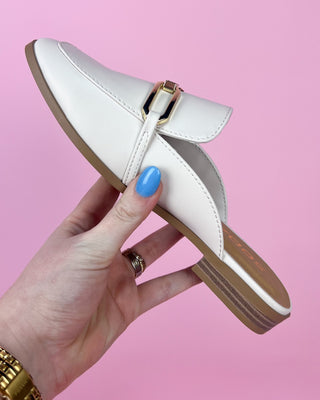 White shoe with a strap held by a hand against a pink background