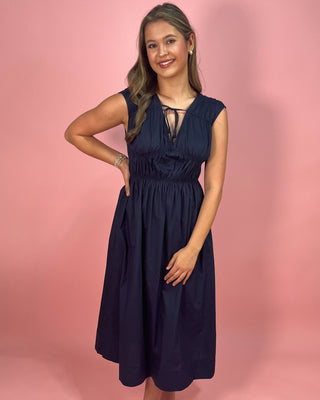 Woman wearing a navy blue dress against a pink background