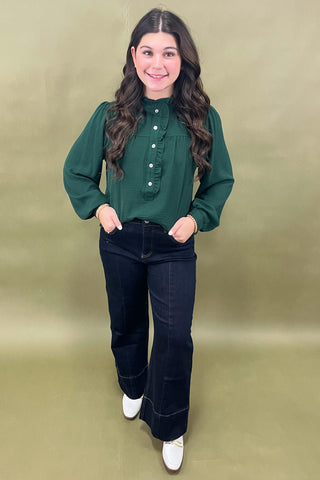 Woman wearing a green blouse and black pants against a beige background