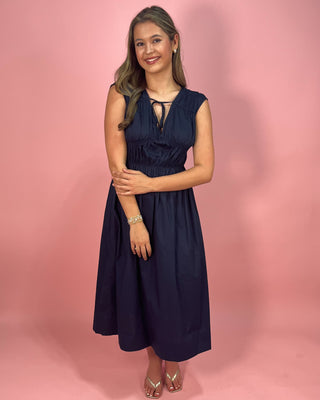 Woman wearing a navy dress against a pink background