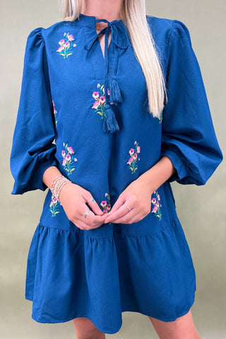 Blue dress with floral embroidery and tassel details on a plain background