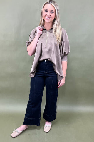 Woman wearing a beige blouse and black pants against a plain background