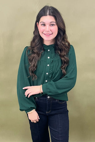 Woman wearing a green blouse with long sleeves against a beige background
