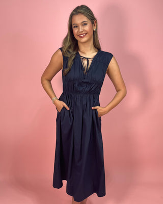 Woman wearing a navy dress against a pink background