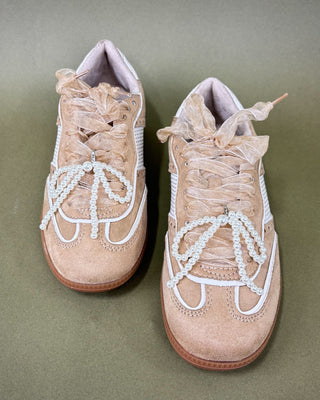Pair of beige sneakers with white beaded laces on a green background