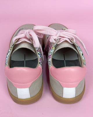Pair of pink and gray sneakers with embellished laces on a pink background