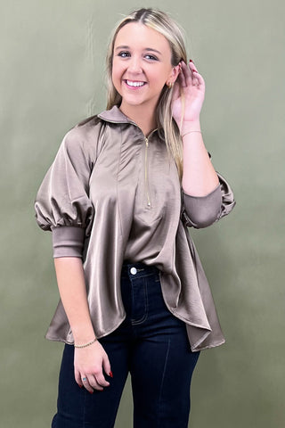 Woman wearing a beige blouse with long sleeves against a green background