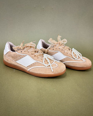 Pair of beige sneakers with white accents on a green background