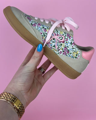Floral-patterned sneaker with pink accents held by a hand against a pink background