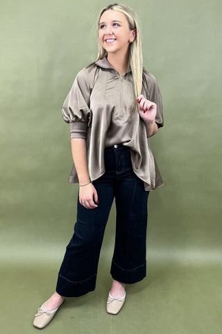 Woman wearing a beige blouse and dark pants against a green background