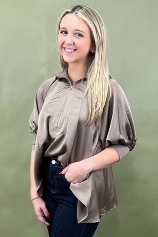 Woman wearing a beige long-sleeve top with a zipper on a green background