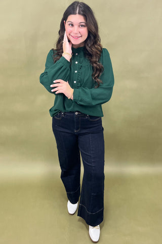 Woman wearing a green blouse and dark jeans on a beige background