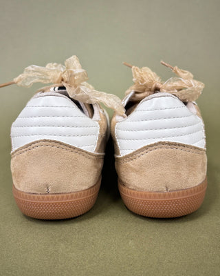 Pair of white and beige sneakers with ribbons on a green background
