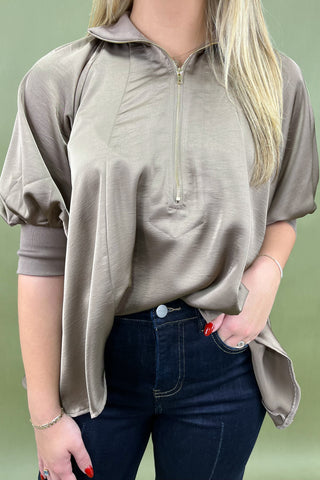 Person wearing a beige zip-up shirt and dark jeans against a green background