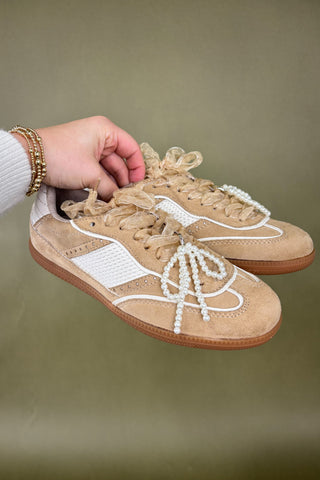 Beige sneakers with white laces held by a hand against a green background